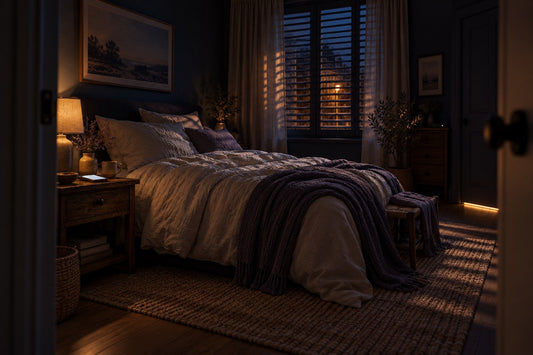 Chambre vue depuis la porte à la nuit tombée : lit, lampe de chevet allumée, lumière de la rue entre les volets