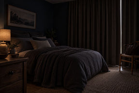 Chambre sombre en plein jour, rideaux occultants tirés avec un mince filet de soleil, lit fait, sac posé sur une chaise