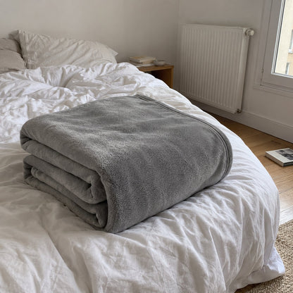 Plaid tout doux gris plié au bout d'un lit